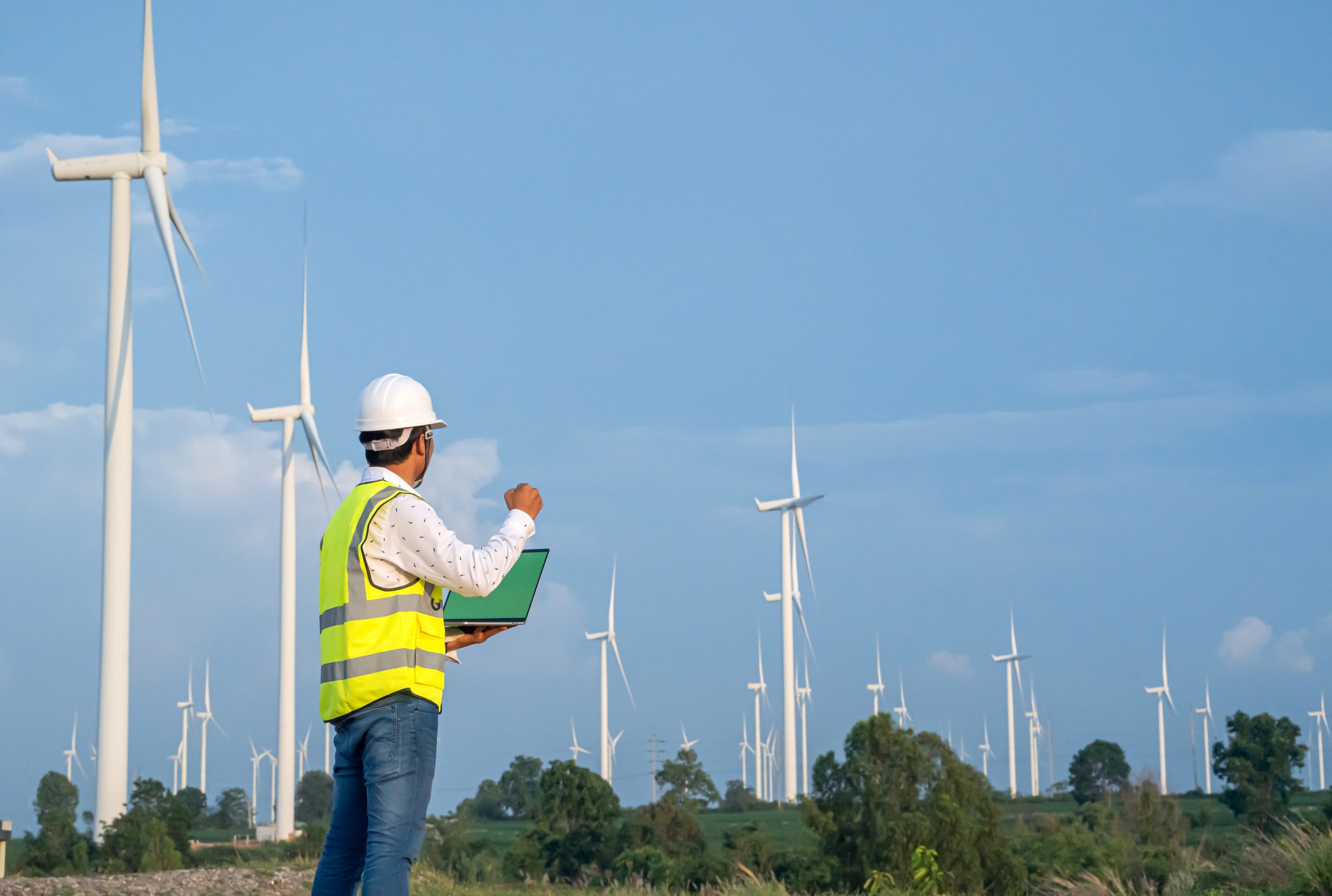 A man in a hard hat standing in front of a field of wind turbines